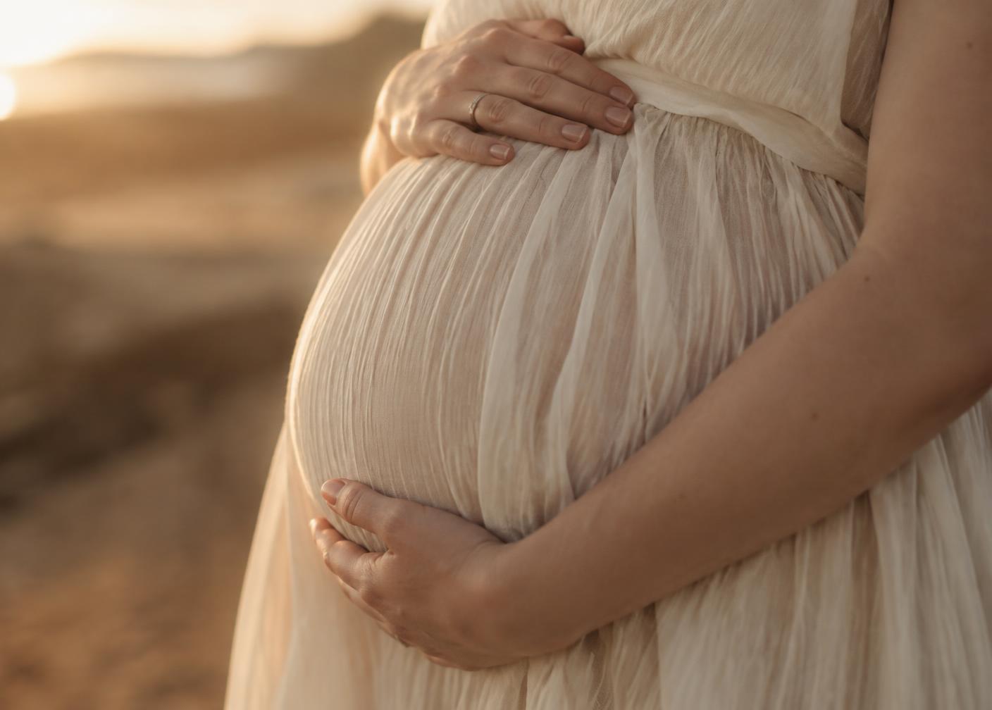 Detalhe das mãos de uma gestante repousando sobre a barriga